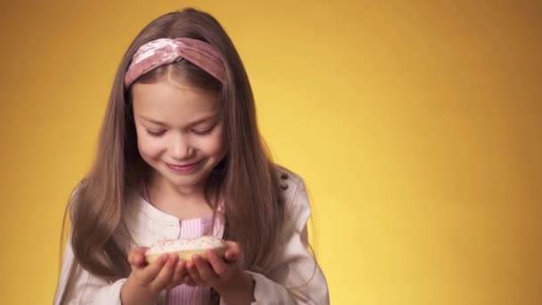 Το κοριτσάκι τρώει ντόνατς σε κίτρινο φόντο. ένα παιδί απολαμβάνει γλυκά — Αρχείο Βίντεο