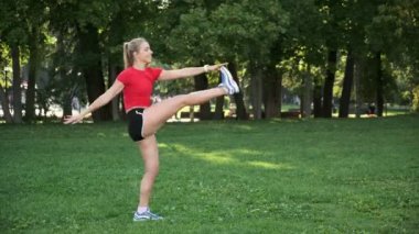 Genç bir kız spor için doğaya gider. Egzersiz ve açık havada esneme. Parkta koşuya hazırlık. Sarışın