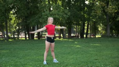 Genç bir kız spor için doğaya gider. Egzersiz ve açık havada esneme. Parkta koşuya hazırlık. Sarışın