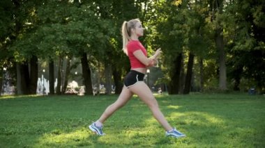 Genç bir kız spor için doğaya gider. Yoga yapıyorum. Kadın arkaya doğru uzanıyor ve parkta ileri doğru hamle yapıyor.