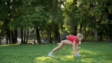 Genç bir kız spor için doğaya gider. Yoga yapıyorum. Kadın arkaya doğru uzanıyor ve parkta ileri doğru hamle yapıyor.