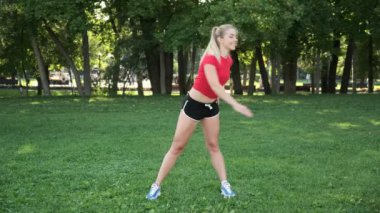 Genç bir kız spor için doğaya gider. Egzersiz ve açık havada esneme. Parkta koşuya hazırlık. Sarışın