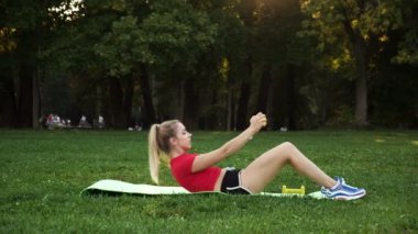 a young woman in a red T-shirt is engaged in fitness outdoors, the girl does an exercise on the abdominals in nature.