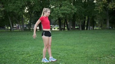 Genç bir kız spor için doğaya gider. Egzersiz ve açık havada esneme. Parkta koşuya hazırlık. Sarışın