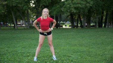 Genç bir kız spor için doğaya gider. Egzersiz ve açık havada esneme. Parkta koşuya hazırlık. Sarışın