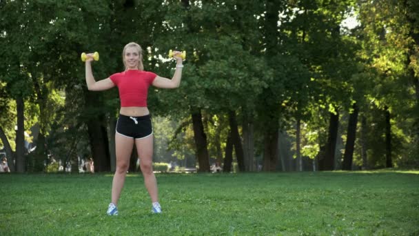 La muchacha joven entra para los deportes en la naturaleza con las mancuernas. gimnasio rubio entrenamiento al aire libre. — Vídeo de stock