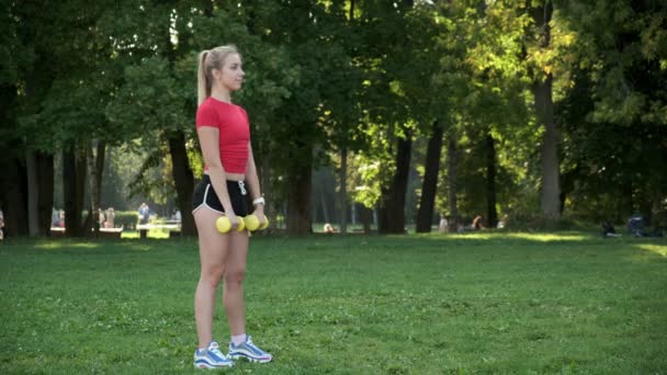 La muchacha joven entra para los deportes en la naturaleza con las mancuernas. gimnasio rubio entrenamiento al aire libre. — Vídeos de Stock