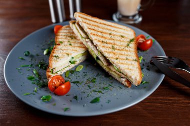 Kızarmış tavuk göğsü ve salata sandviçi. Kahverengi bir kağıda sarılmış, ahşap bir masada servis ediliyor.