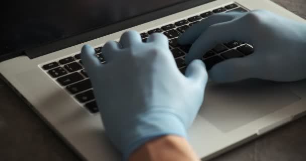 Молодой индийский бизнесмен носит медицинские перчатки, работающие на ноутбуке, сидя за столом домашнего офиса. — стоковое видео