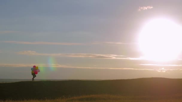 Sziluettjét lány séta léggömbökkel a mező, a naplemente. Boldog gyermek léggömbökkel naplemente alatt szereplő.