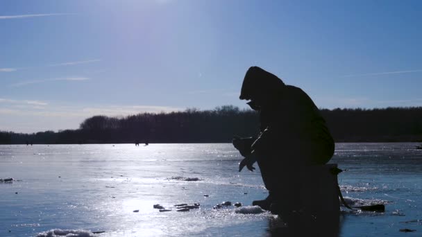 Silhouette fisherman on ice at frozen lake in winter. Winter holidays and people hobby concept. — Stock Footage Silhouette fisherman on ice at frozen lake in winter. Winter holidays and people hobby concept. Stock Footage