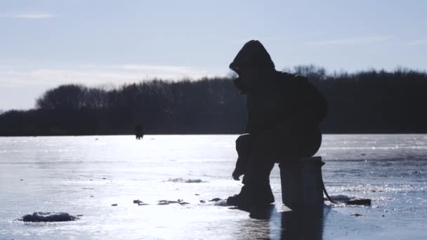 Silhouette fisherman on ice at frozen lake in winter. Winter holidays and people hobby concept. — Stock Footage Silhouette fisherman on ice at frozen lake in winter. Winter holidays and people hobby concept. Video Clip