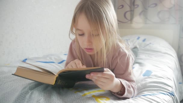 Girl child lay bed read book. Girl kid long hair cute pajamas relax and read fairytale book. Pleasant time in cozy bedroom.