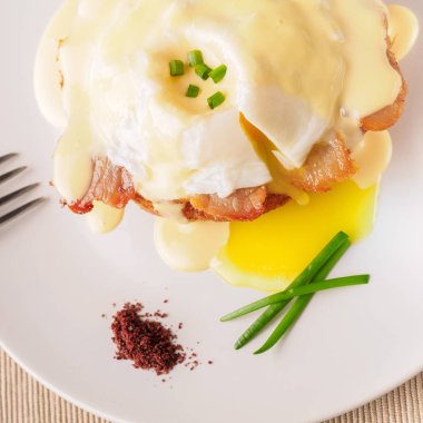 Kahvaltı Yumurta Benedict - tost İngilizce muffins, pastırma, jambon, haşlanmış yumurta, otlar ve lezzetli tereyağı hollandaise sos var. Beyaz tabak ve çatal. Üstten görünüm. Metin için yer.