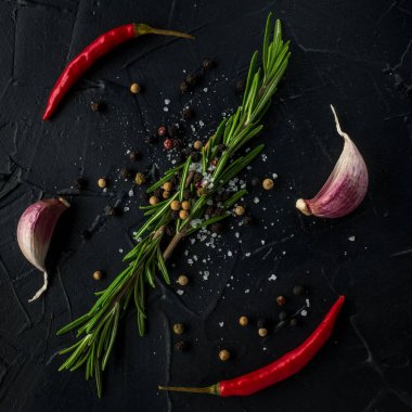 Kırmızı sıcak biber biber, sarımsak ve biberiye deniz tuzu ve siyah arka plan üzerinde renkli biber ile