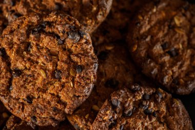 Rustik koyu siyah arka plan üzerine çikolatalı kurabiye. Çikolatalı kurabiye kahverengi peçete üzerinde yığılmış. Sembolik görüntü metin için yer ile. Fırından yeni çıkmış. Lezzetli bir aperatif için kavram. Şekerli tatlı. Seçici odak. Yakın çekim.