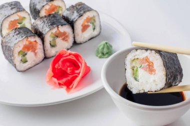 Suşi yemek çubukları, soya soslu, closeup içeri girin. Plaka rulo Japon deniz ürünleri suşi zencefil ve arka plan üzerinde wasabi ile.