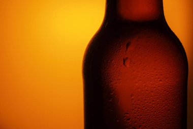 Şişe bira turuncu bir arka plan üzerinde damla ile. Şişe parçası kadar kapatın. Soğuk bira şişesi bardak kadar kapatın.