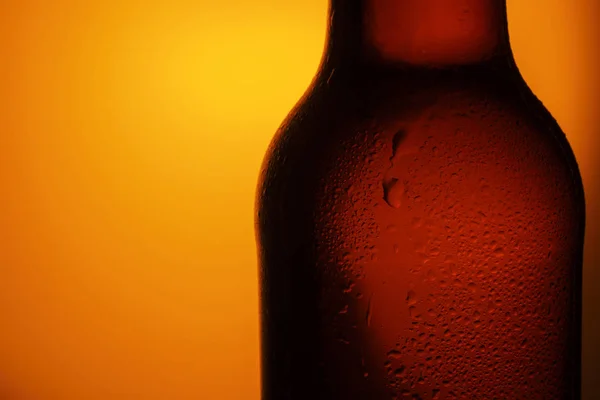 Bottle of beer with drops on a orange background. Close up part of the bottle. Close up shot of frosty beer bottle.