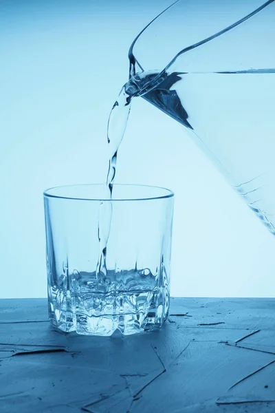 Pour water from a pitcher into a glass. Drinking water is poured from a jug into a glass on a blue background.