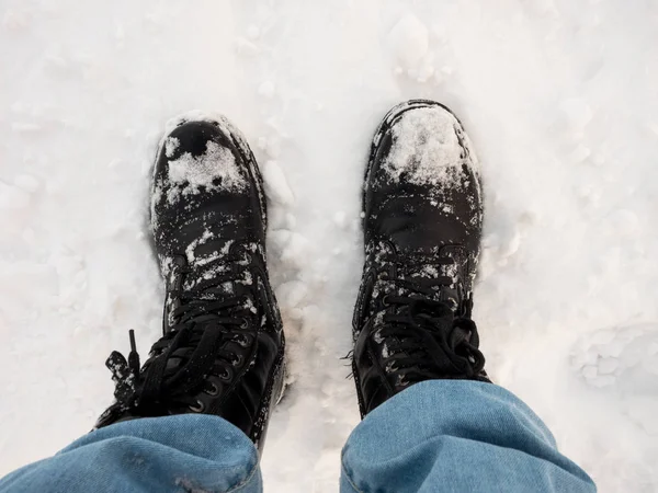 feet in black trekking boots on snow, a trip in winter, a picture from above.