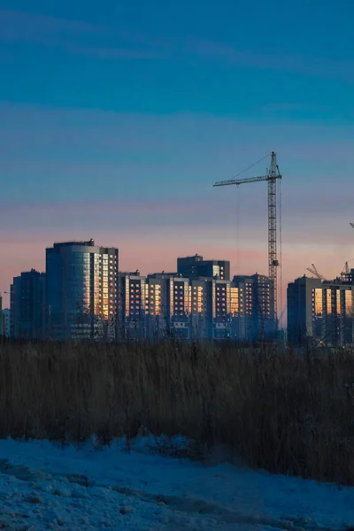 Building crane and modern buildings under construction against evening sky. Sunset sky.