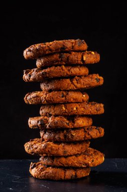Rustik koyu siyah arka plan üzerine çikolatalı kurabiye. Çikolatalı kurabiye kahverengi peçete üzerinde yığılmış. Sembolik görüntü metin için yer ile. Fırından yeni çıkmış. Lezzetli bir aperatif için kavram. Şekerli tatlı. Seçici odak. Yakın çekim.