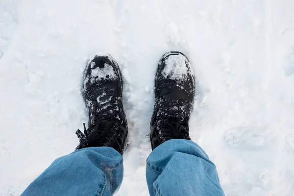 feet in black trekking boots on snow, a trip in winter, a picture from above.