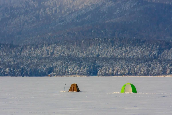 tents for winter fishing on a huge mountain lake. winter landscape. pure white snow. Fishermen catch fish in the fresh air. people\'s hobbies and sports