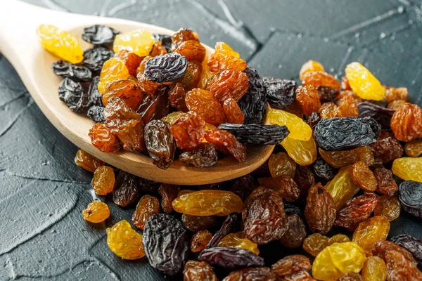 Assortment of Raisins, yellow, blue, black, golden raisin in wooden spoon scattered on dark table of kitchen. Healthy snack, dietary product for good life. copy space, Vega Food