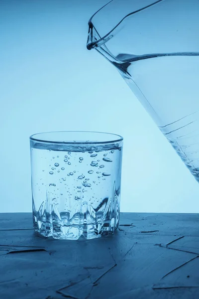 Pour water from a pitcher into a glass. Drinking water is poured from a jug into a glass on a blue background.