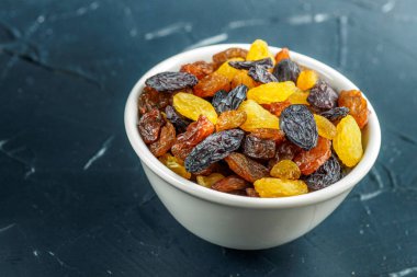 Ürün çeşitliliği, Kuru üzüm, sarı, mavi, siyah, altın kuru üzüm siyah arka plan üzerine beyaz seramik kase. Sağlıklı snack. Vega gıda. Gıda mix arka plan, üstten görünüm, kopya alanı, afiş.