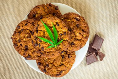 Delicious homemade Chocolate chip Cookies with CBD cannabis and leaf garnish and buds. Medicinal Edibles. Treatment of medical marijuana for use in food. Canada legalization. Rasta cookie recipe. Marijuana and biscuit. Reggie food. Narcotic sweets. J clipart