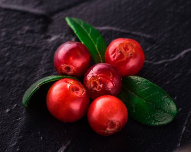 Fuska (foxberry, İsveç kirazı). Üstten görünüm. Vahşi kızılcık rustik koyu arka plan üzerinde. Olgun kırmızı orman Vaccinium vitis-idaea yeşil yaprakları ile çilek. Kopya alanı.