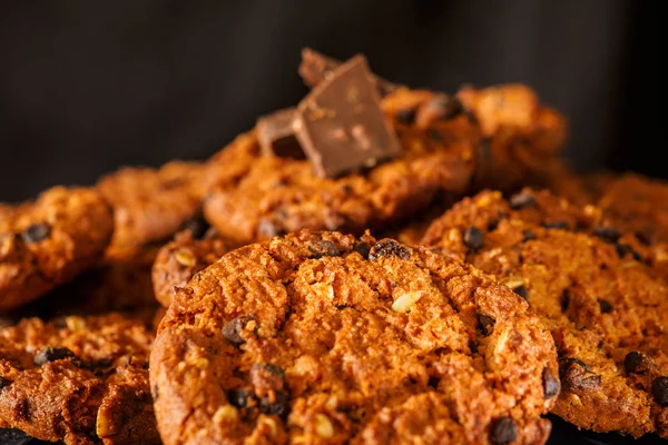 Chocolate chip cookies on rustic dark black background. Stacked chocolate chip cookies on brown napkin. Symbolic image with place for text. Freshly baked. Concept for a tasty snack. Sweet dessert. Selective focus. Close up.