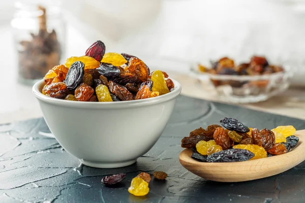 Ceramic bowl with Assortment of Raisins, yellow, blue, black, golden raisin and wooden spoon on table of kitchen. Healthy snack, dietary product for good life. copy space, Vega Food