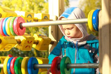 Sevimli 3 yaşındaki çocuk heyecanla serin bahar günü açık havada oyun oynuyor. Çocuk eğlence salıncak, kum, carousel ve eğlence parkı içindeki slaytları karmaşık.