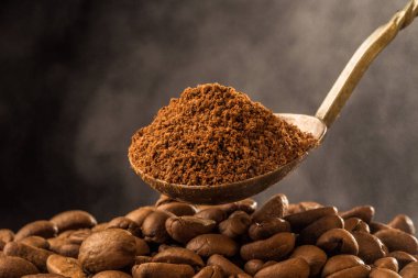 Kavrulmuş toprak içine eski bir gümüş kaşık ve kavurma kahve çekirdekleri koyu arka plan üzerinde duman buhar ile kahve. Yakın çekim fotoğraf. Kopya alanı Vintage tarzı etkisi resimle.