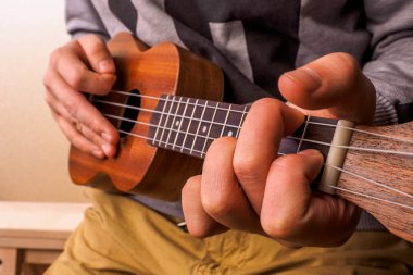 Akustik gitar ukulele oynayan genç adam closeup eller.