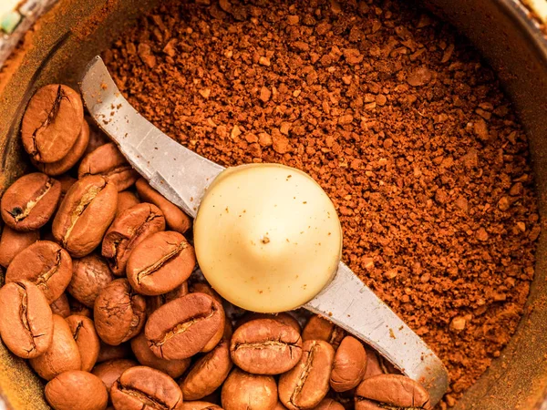 Macro photo of freshly ground coffee in electric coffee grinder with roasted coffee beans inside and coffee grains close-up view of the top.