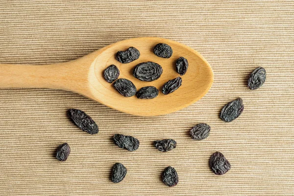 Blue Raisins in wooden spoon on textile background on the kitchen. Healthy snack, dietary product for good life. copy space, Vega Food. Close-up image. Macro. Top view.