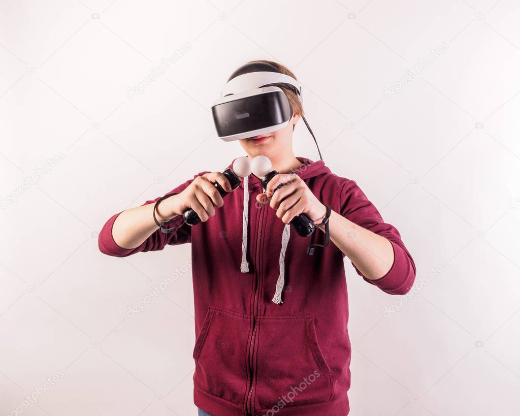 Young male model looking through virtual reality (VR) headset with handheld controllers isolated on white background. 