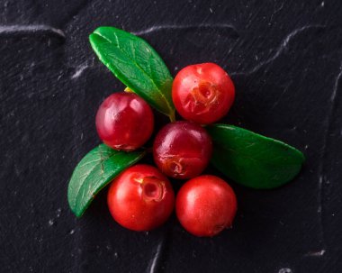 Fuska (foxberry, İsveç kirazı). Üstten görünüm. Vahşi kızılcık rustik koyu arka plan üzerinde. Olgun kırmızı orman Vaccinium vitis-idaea yeşil yaprakları ile çilek. Kopya alanı.