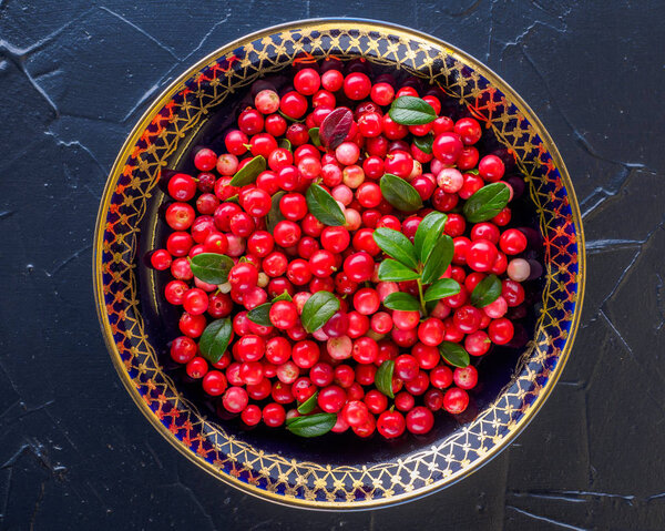 Berries on a plate on a dark background in a rustic style. National cuisine. raw materials for tea, jam and medicinal decoctions. Vaccinium vitis-idaea (lingonberry or cowberry).