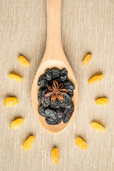 Blue Raisins in wooden spoon and anise on textile background on