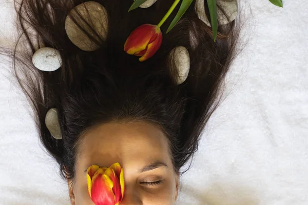 Young girl\'s hair twisted with spa stones and tulips.