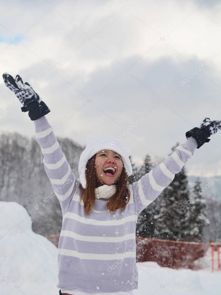 Happy asian woman enjoys winter, playing with snow, a woman throws white, loose snow into the air. Beauty woman having fun in winter park