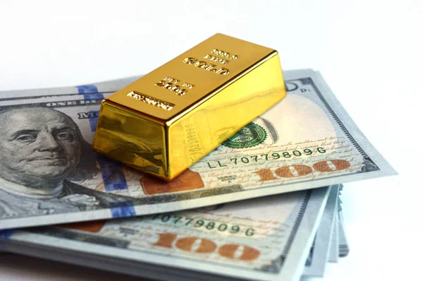 Closeup view of a stack of hundred dollar american bills with a fine gold ingot resting on top.