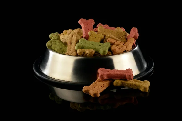 An overwhelming amount of dog treats inside a feeding dish over a black background.