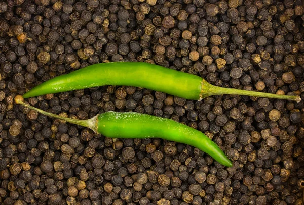 green fresh green chili two parallel pods on a background of black peppercorns base design culinary contrast